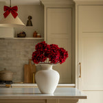 Kitchen with a vase of red flowers on a counter, wooden stools, and neutral color scheme.