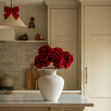 Kitchen with a vase of red flowers on a counter, wooden stools, and neutral color scheme.