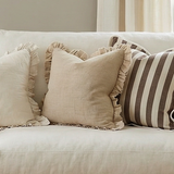 Beige sofa with decorative pillows in a living room setting with large windows and a painting on the wall.