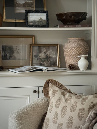 Woven rattan vase styled on painted shelving with framed art, books and a velvet cushion