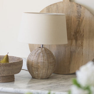 Wicker table lamp with beige shade on a marble surface with decorative elements.