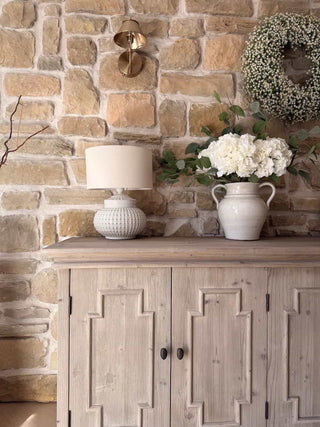 Wooden cabinet with a lamp and vase against a stone wall