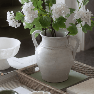 White ceramic vase with greenery and white flowers on a table