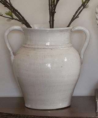 White ceramic vase with handles on a wooden surface against a neutral background