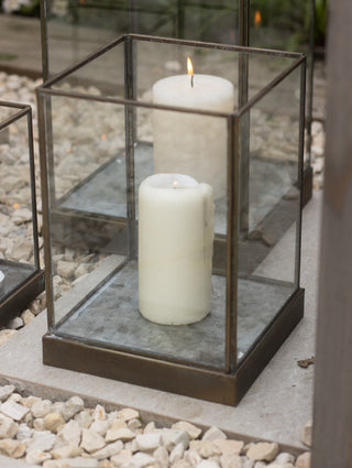  Single large Whitstable hurricane lantern with a lit white pillar candle inside, showing the bronze metal frame and clean glass panels