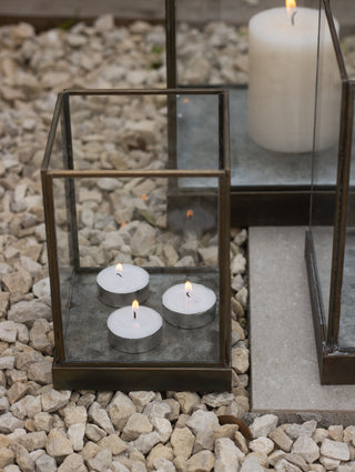 Small Whitstable hurricane lantern filled with three lit tealights on a paved outdoor step