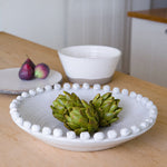 White ceramic bobble bowl styled with artichokes on a wooden table