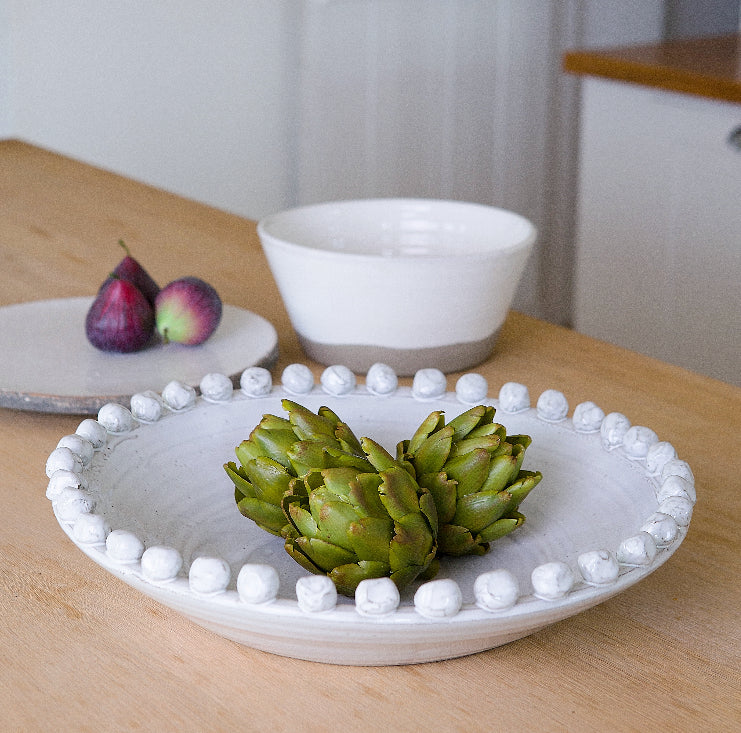 White ceramic bobble bowl styled with artichokes on a wooden table