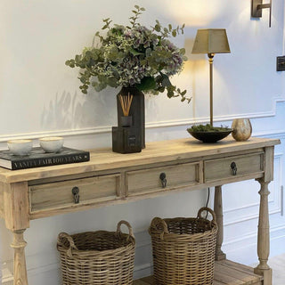 Wooden console table with decorative items including a vase of flowers, books, and baskets.