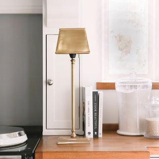 Gold lamp on a wooden surface with books and a jar in the background