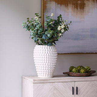 White textured vase with greenery on a wooden cabinet against a neutral wall.